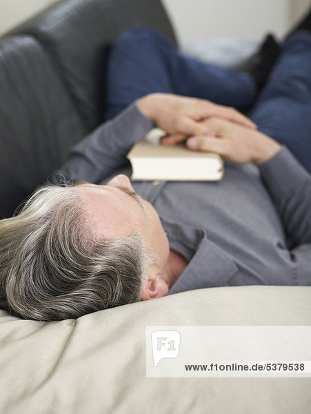 Senior man sleeping on sofa with book