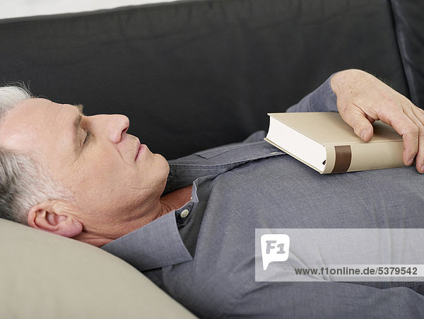Senior Mann schläft auf Sofa mit Buch