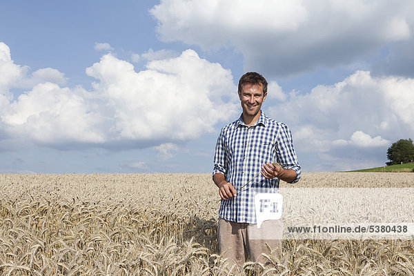 Mann im Weizenfeld stehend  lächelnd  Portrait
