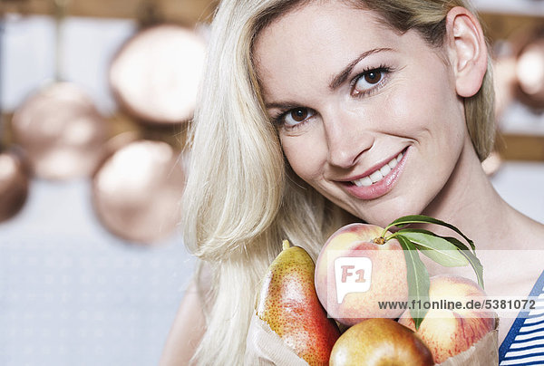 Italien  Toskana  Magliano  Junge Frau hält Früchte in der Küche  lächelnd  Portrait