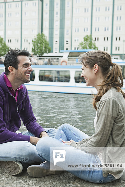 Germany  Berlin  Couple sitting face to face on riverbank