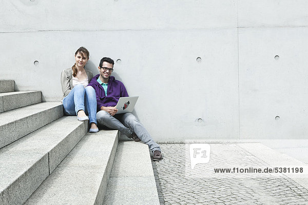 Germany  Berlin  Couple using laptop on stairway