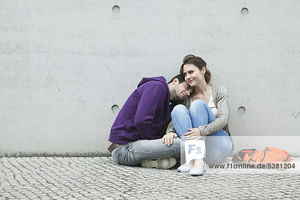 Germany  Berlin  Couple sitting in front of large wall on sidewalk