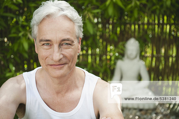 Reifer Mann lächelnd mit Buddha-Statue im Hintergrund