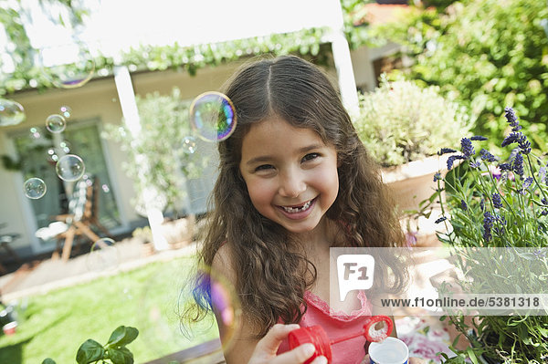 Mädchen bläst Seifenblasen im Garten  lächelnd  Portrait