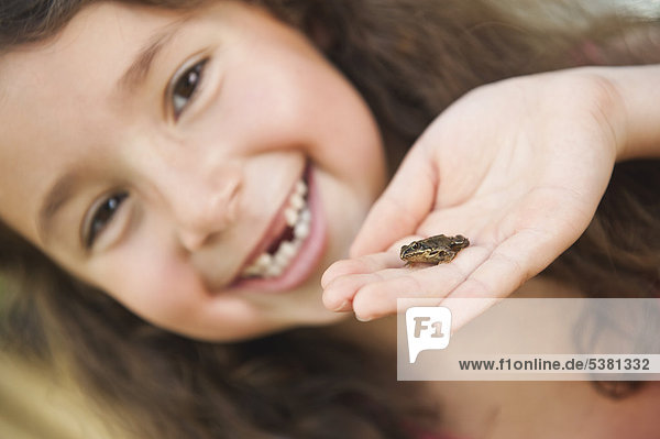 Menschliche Hand mit kleinem Frosch  Mädchen lächelnd im Hintergrund