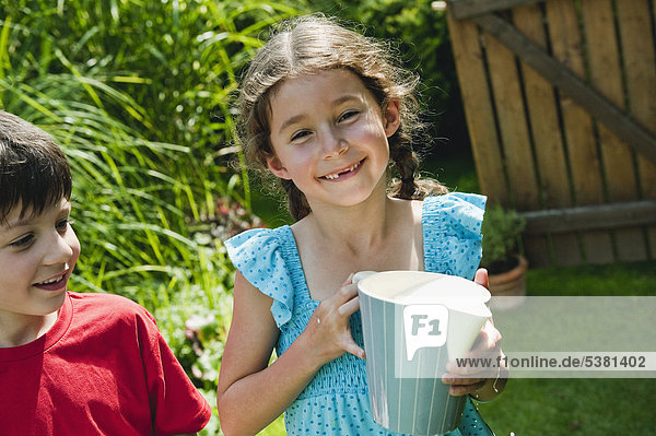 Girl holding pitcher with boy smiling