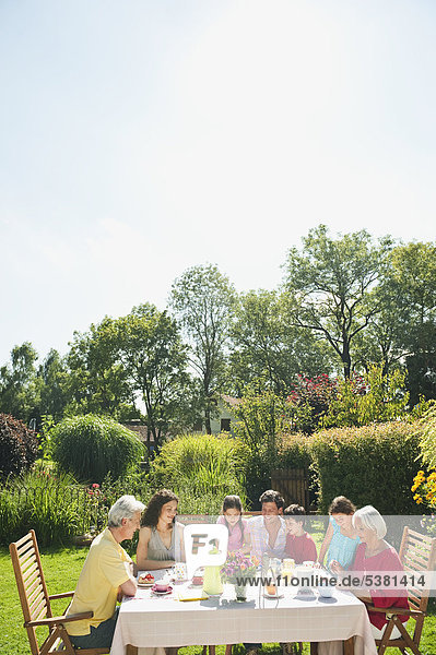 Germany  Bavaria  Family having coffee and cake in garden  smiling