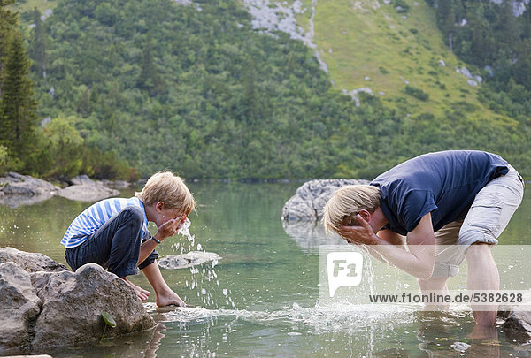 Boy washing his face in still lake