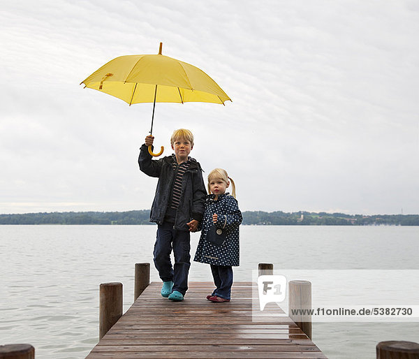 Children with yellow umbrella on dock