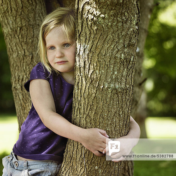Lächelndes Mädchen umarmt Baum