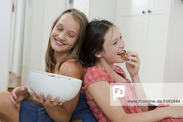 Lächelnde Mädchen essen Brezeln im Schlafzimmer