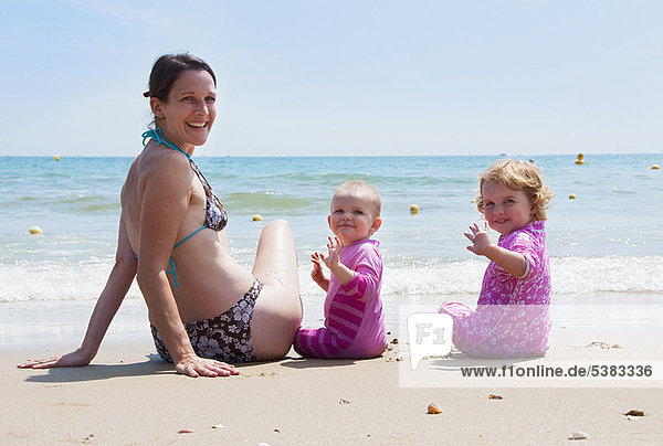 Mother sitting on beach with daughters