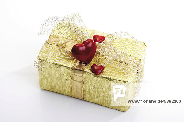 Goldenes Geschenkpäckchen mit Schleife und roten Herzen