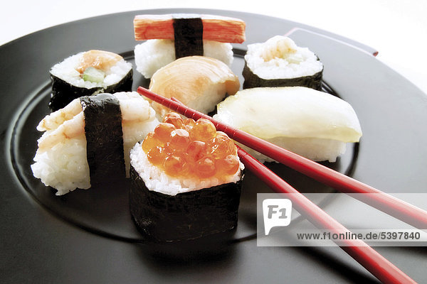Sushi Vielfalt auf schwarzem Teller mit Essstäbchen