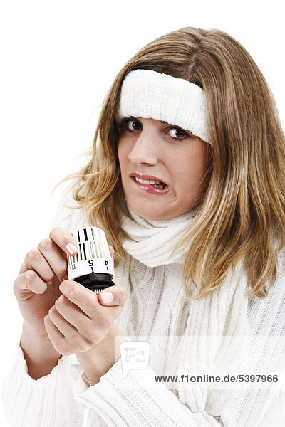 Freezing young woman in a white turtleneck sweater with headband holding thermostat