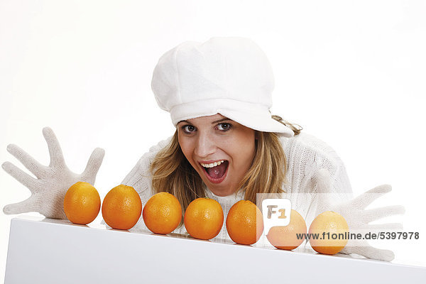 Young woman in a white turtleneck sweater with woolen hat  oranges in a row in front