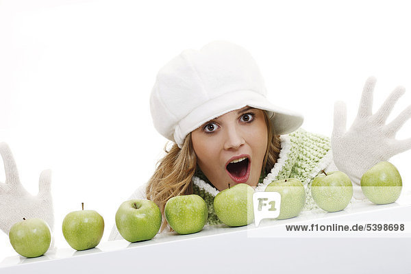 Young woman wearing a scarf and a cap  behind a row of green apples