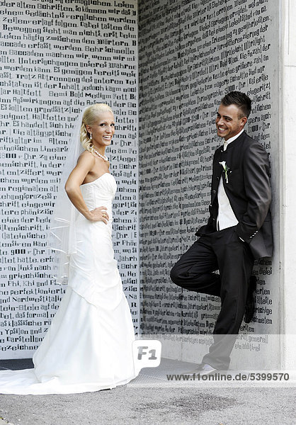 Hochzeit  Braut und Bräutigam lachen und stehen vor einer Wand mit Schriftzeichen