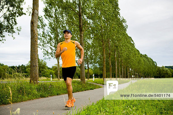 Sportlicher junger Mann joggt auf einer mit Bäumen gesäumten Straße bei Coburg  Bayern  Deutschland  Europa