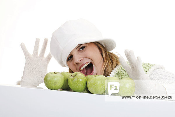 Junge Frau in weißem Pullover und Mütze mit grünen Äpfeln