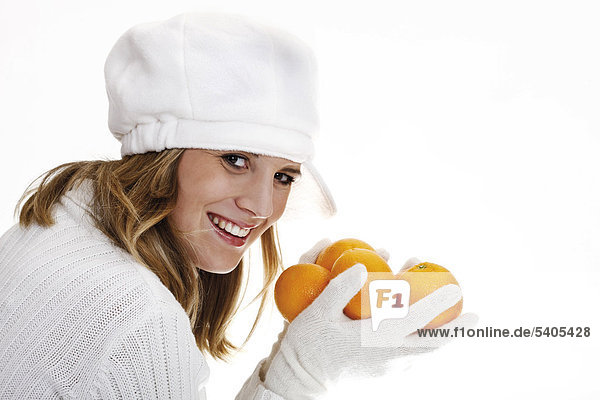 Young woman wearing a white jumper and a hat  holding oranges