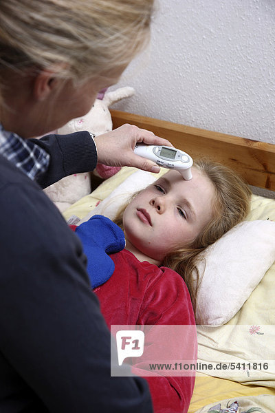 Girl  10 years old  is ill in bed with a cold  flu  fever  her mother taking the temperature with a digital skin thermometer