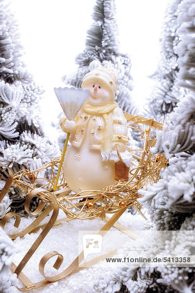 Snowman figure sitting on a golden sleigh in a snowy forest