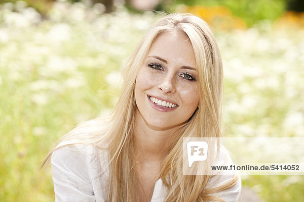 Junge blonde Frau sitzt lächelnd auf einer sommerliche Wiese