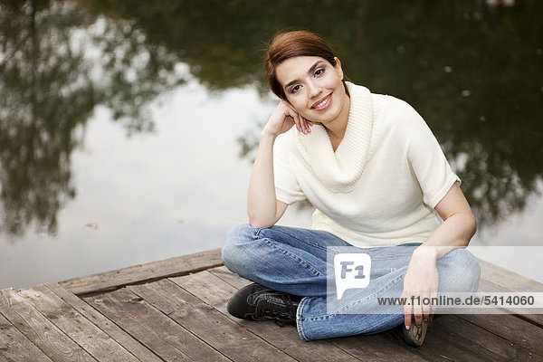 Junge Frau sitzt freundlich lächelnd auf einem Steg am See