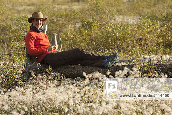 Young woman relaxing  enjoying evening light  sitting on a tree trunk  Cotton Grass  Wind River  Yukon Territory  Canada
