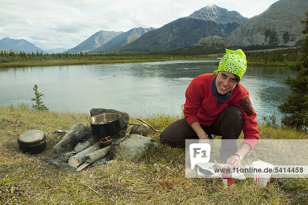 Young woman cooking on a camp fire  cutting up mushrooms  camping  Mackenzie Mountains behind  Wind River  Peel Watershed  Yukon Territory  Canada