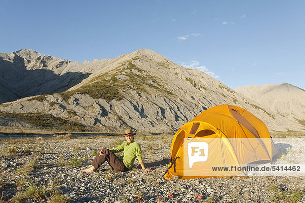 Young woman sitting  relaxing  enjoying the evening light  expedition tent  arctic tundra  camping  Mackenzie Mountains behind  Wind River  Peel Watershed  Yukon Territory  Canada