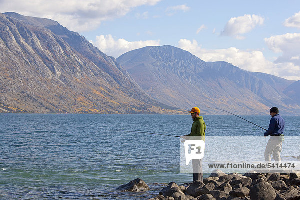 Two men spin fishing  Kusawa Lake  mountains behind  Indian summer  leaves in fall colours  autumn  Yukon Territory  Canada