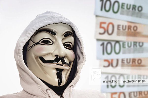 Man wearing the Guy Fawkes mask used by the Occupy movement beside euro banknotes  protesting against the power of banks