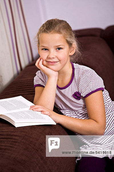 8-jähriges Mädchen sitzt mit Buch auf Sofa