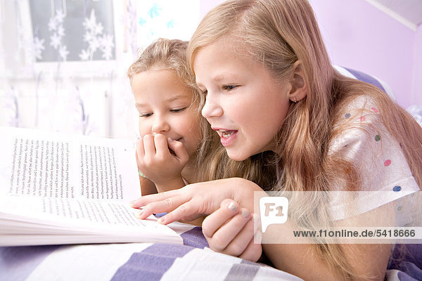 Two girls  sisters reading in bed
