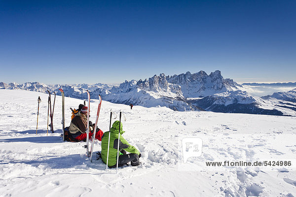 Ski tourers taking a break on the summit of Mt Uribrutto  above Passo Valles  Dolomites  Pale di San Martino mountains and the Passo Rolle in the back  Trentino  Italy  Europe