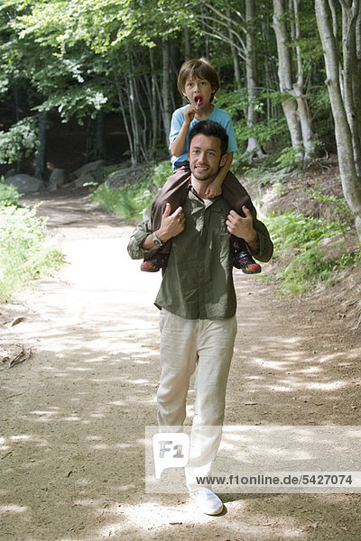 Vater trägt den Sohn auf den Schultern  geht im Wald spazieren.