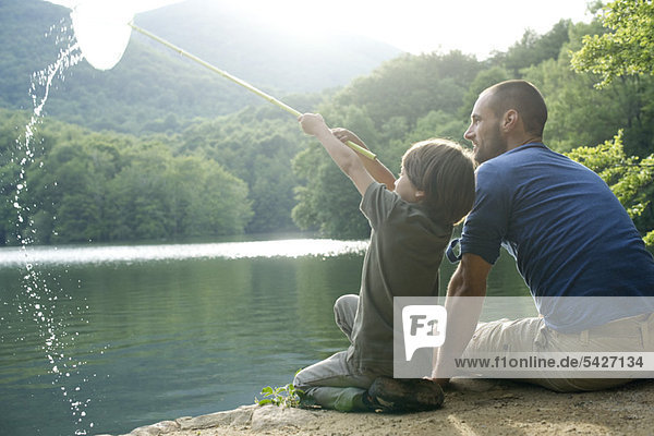 Vater und Sohn beim Fischen  Junge beim Hochhalten des Fischernetzes