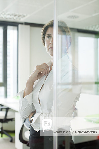 Businesswoman standing behind glass partition in office