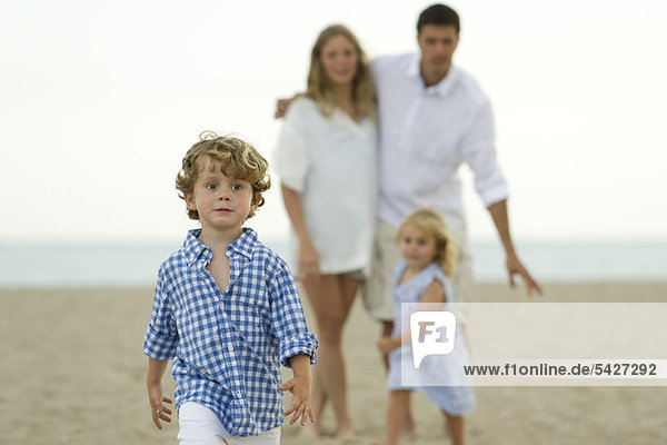 Kleiner Junge  der vor seiner Familie am Strand spazieren geht.