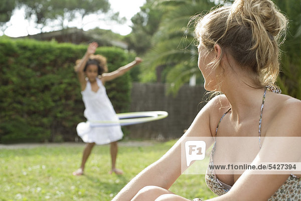 Woman sitting outdoors  watching child playing with plastic hoop