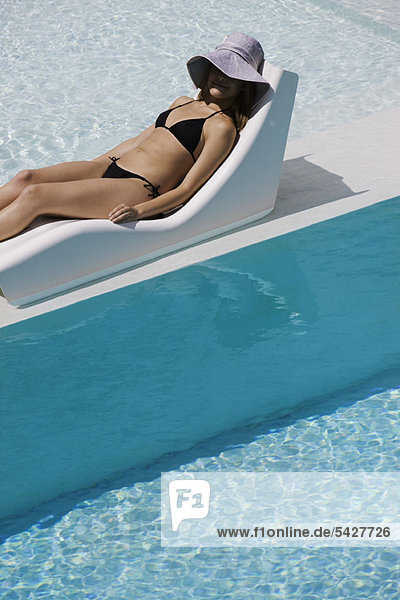 Junge Frau mit Sonnenhut auf dem Liegestuhl am Pool