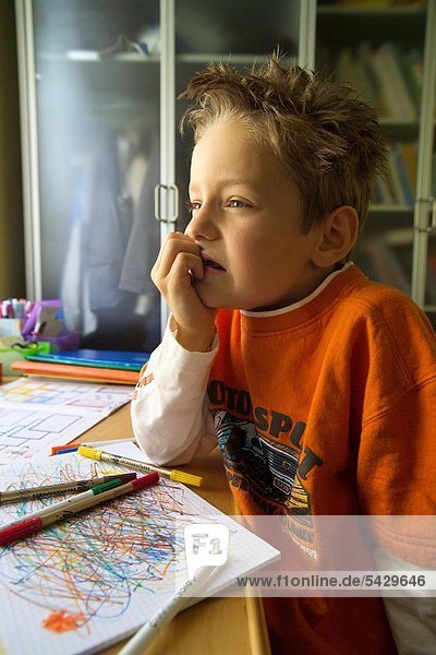 Unruhiger Junge sitzt abwesend vor dem Schreibtisch - ADHS Syndrom