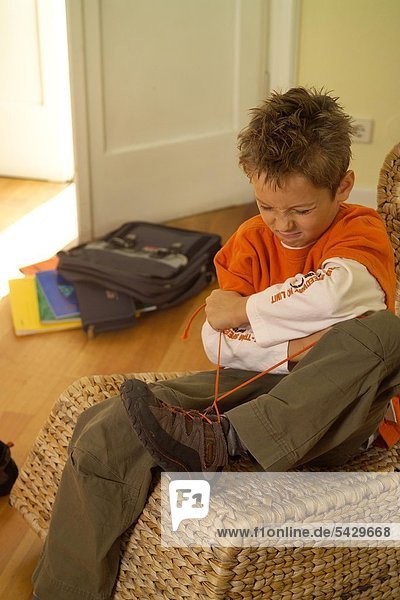Junge sitzt auf einem Sessel und versucht sich die Schuhe zuzubinden - ADHS Syndrom