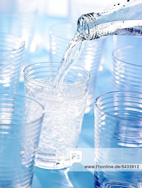 Viele Gläser vor blau - in eines wird aus einer Flasche Wasser geschenkt. CO2 ( Wasser ) - H2O ( Kohlensäure )