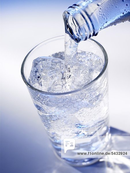 Wasser wird aus einer Flasche in ein Glas mit Eiswürfeln geschenkt - Mineralwasser . CO2 ( Wasser ) - H2O ( Kohlensäure )