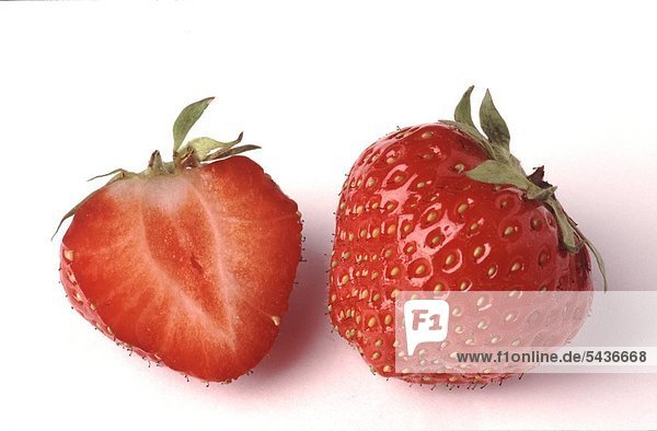 einzelne und halbierte Erdbeere auf weißem Untergrund