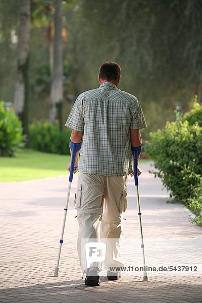 Man with crutches of behind - one with crutches - backview]